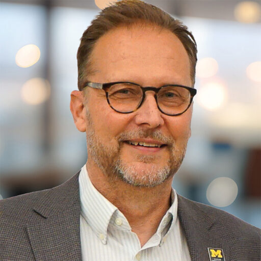 Kurt skifstad headshot a man with light brown hair, glasses and a goatee wearing a brown jacket with a CFE lapel pin