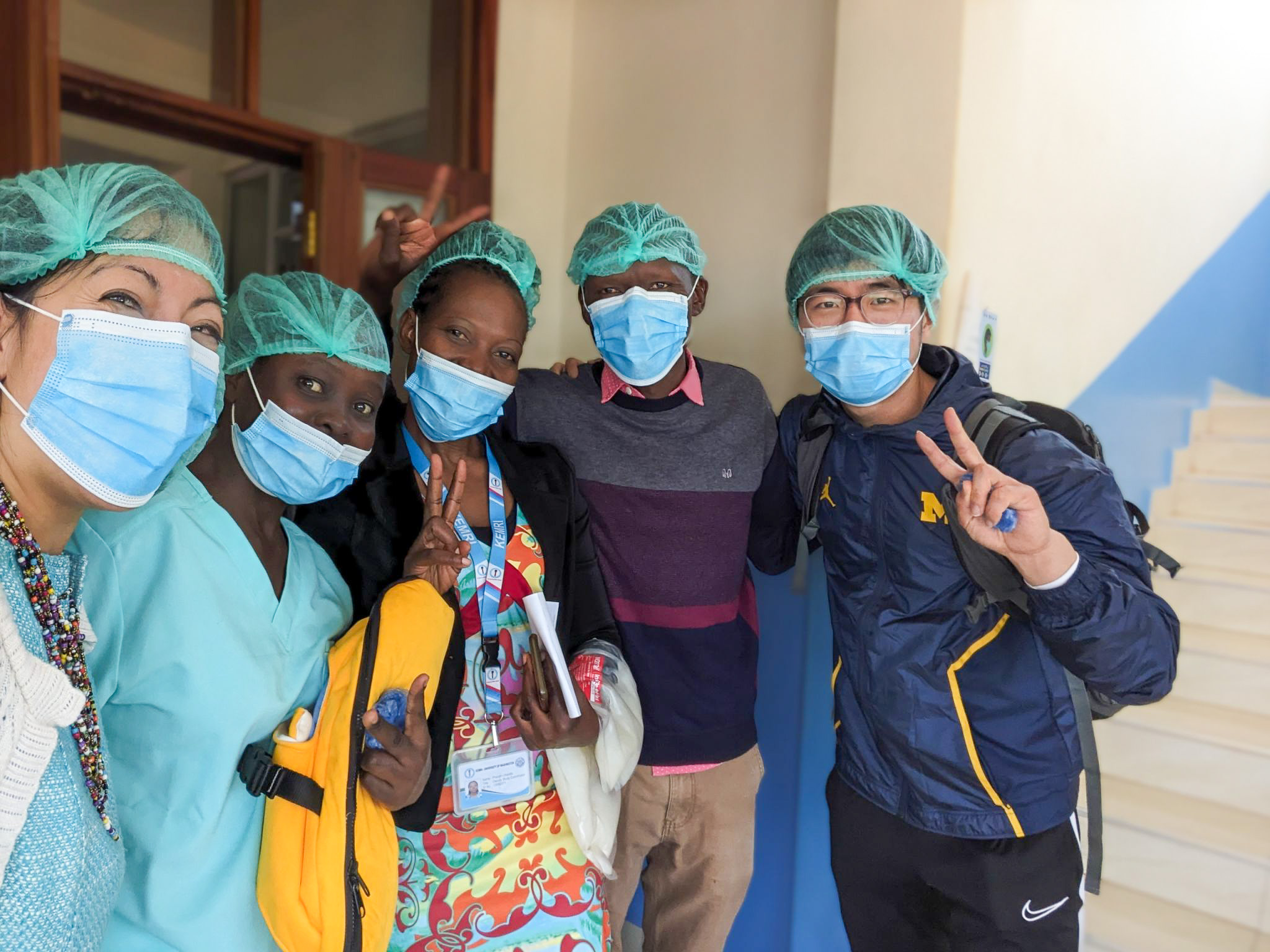 Jooyoung poses with three other people. They are all wearing blue face masks and appear to be hospital staff.