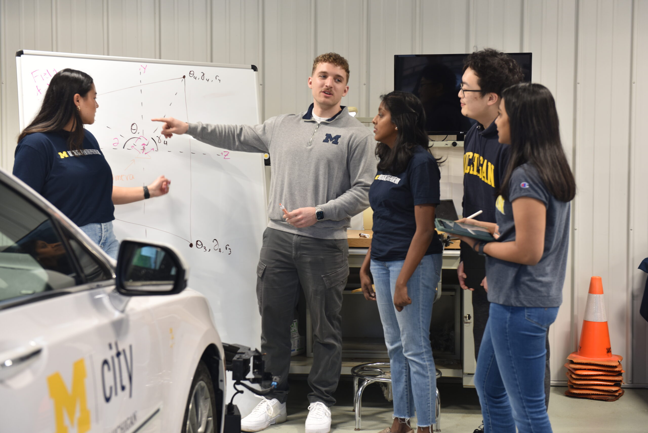 TechLab students work at a whiteboard next to an autonomous vehicle