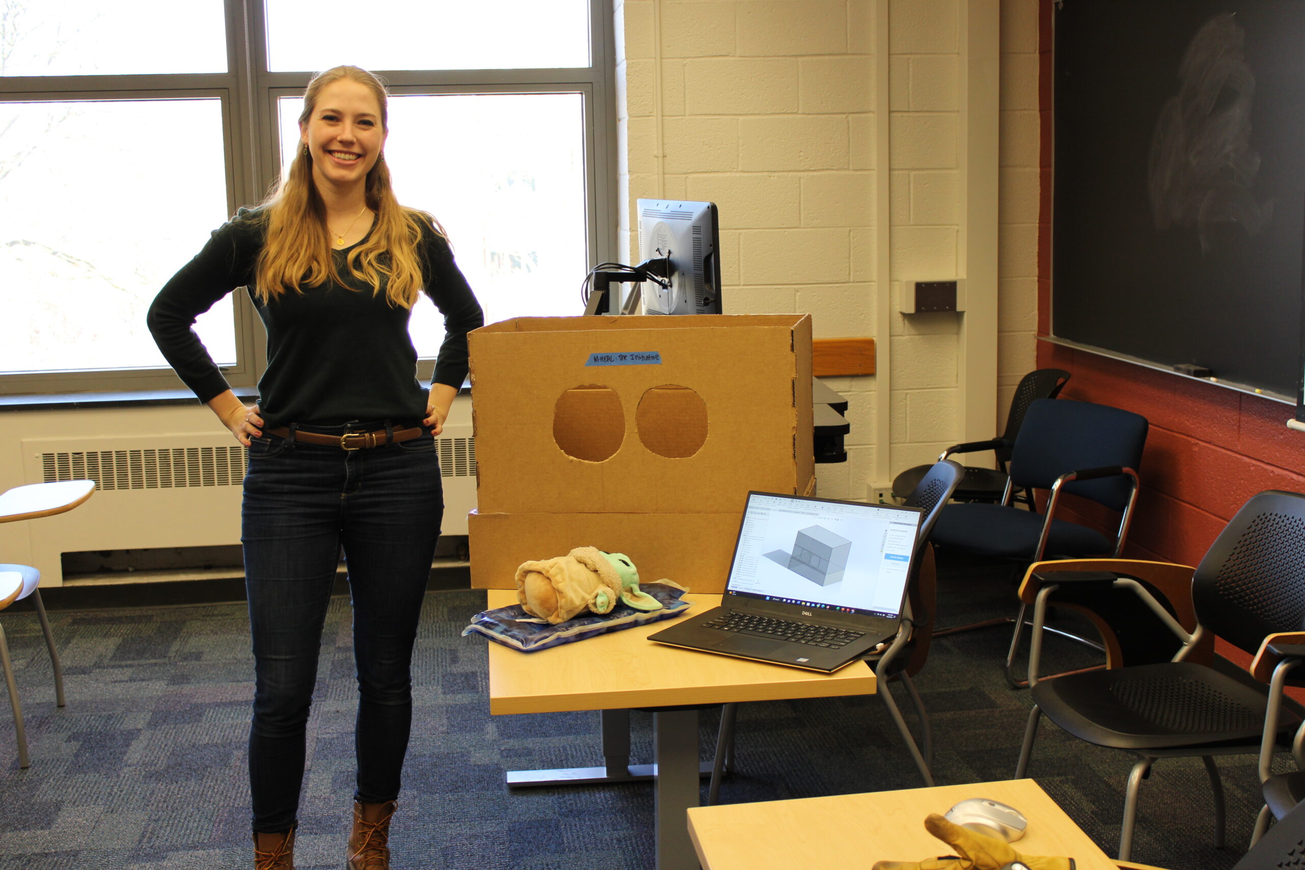 Erin stands next to a cardboard box prototype