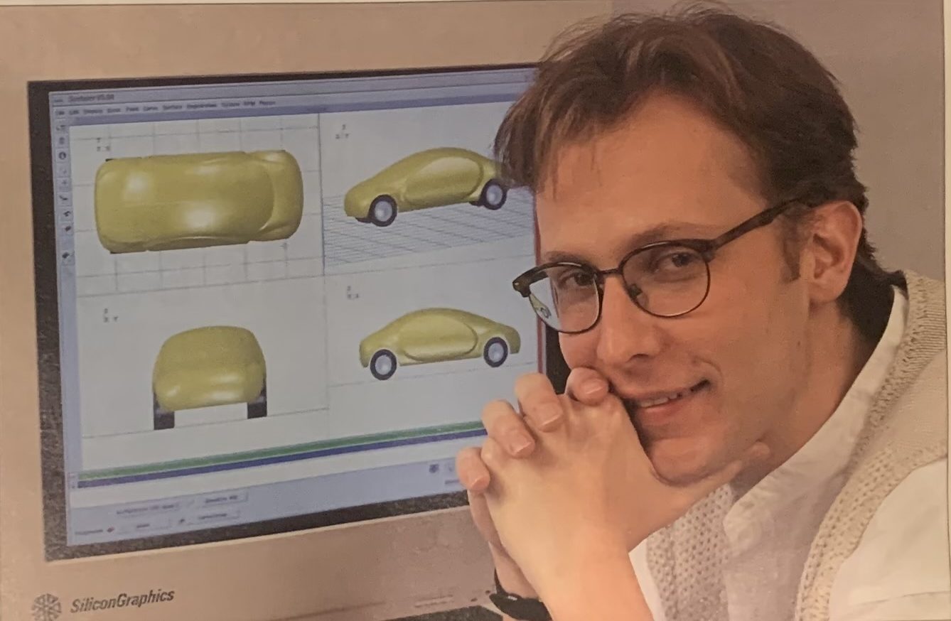 Photo of a photo of a younger Kurt Skifstad next to a computer with a rendering of a futuristic vehicle
