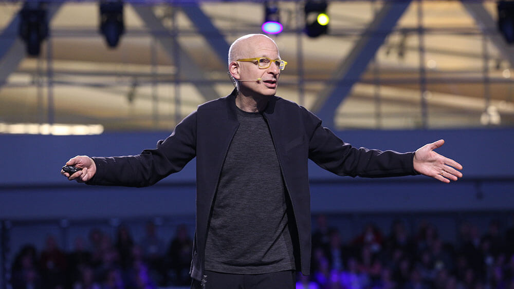 Seth Godin stands on stage speaking at an event