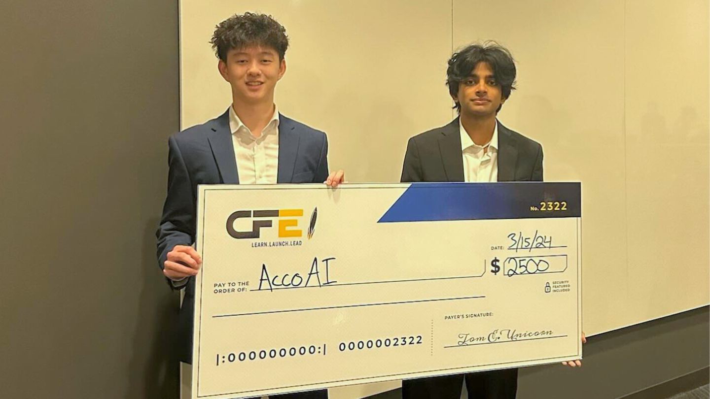 two winning students hold up a giant check