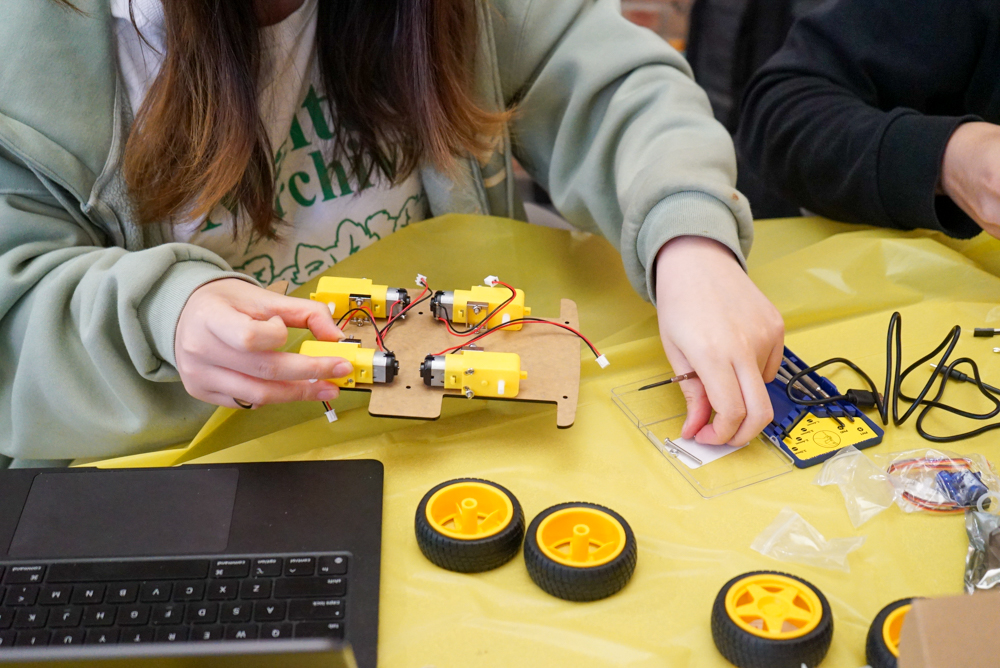 Student hands putting together their robots, gears and tires sitting on the desk