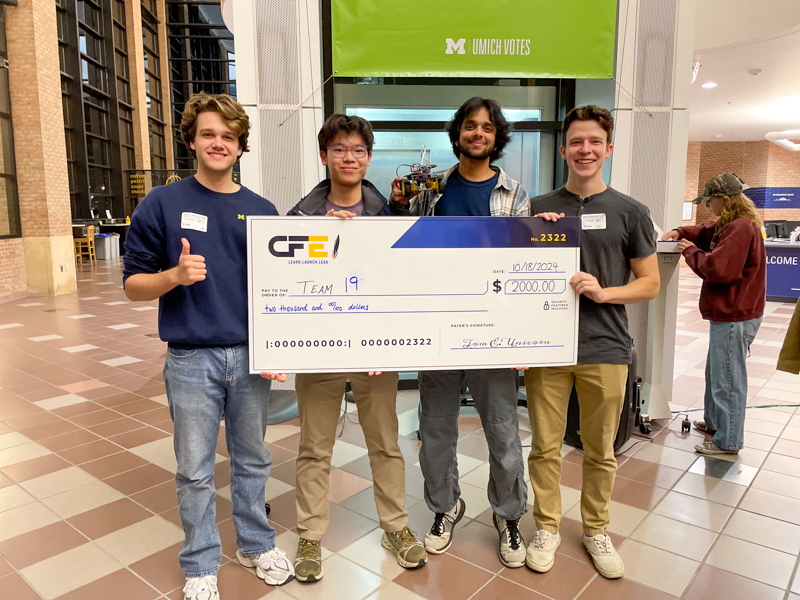 group of four young men smiling standing holding a big check for the win of team 19 for $2000