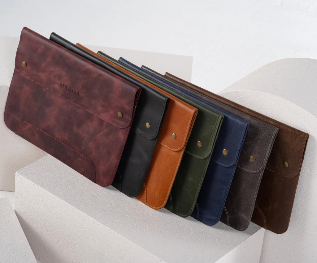 A leather laptop case is shown in 7 variations, with maroon, black, orange, dark green, navy, light brown, and dark brown color options.