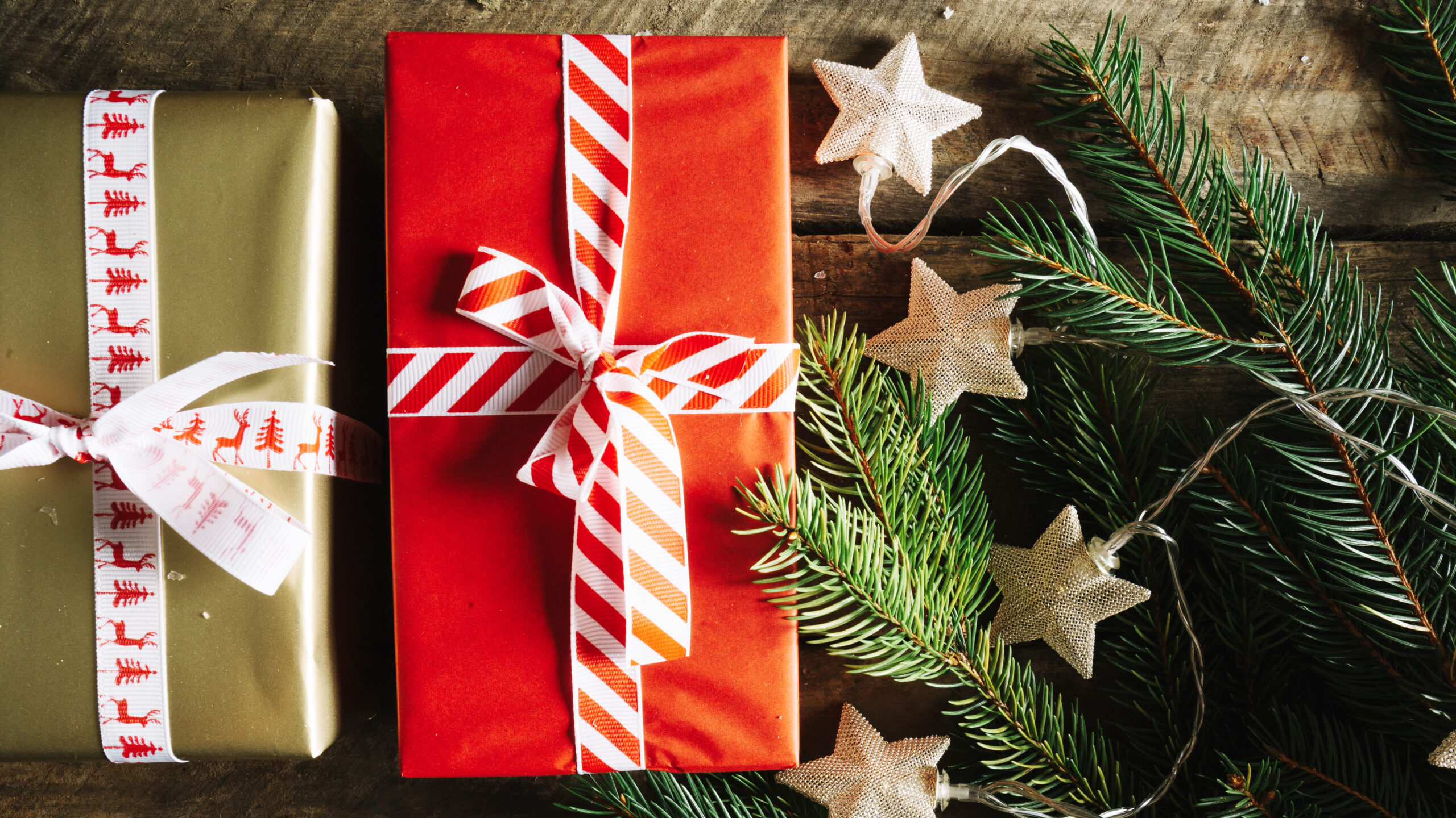 Two christmas gifts are placed on a table, surrounded by fir and glittering stars.