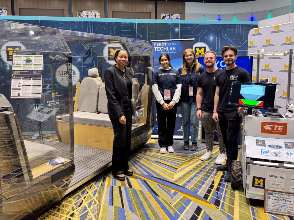 A group of 5 students pose at the PJTL booth at the Detroit Auto Show.