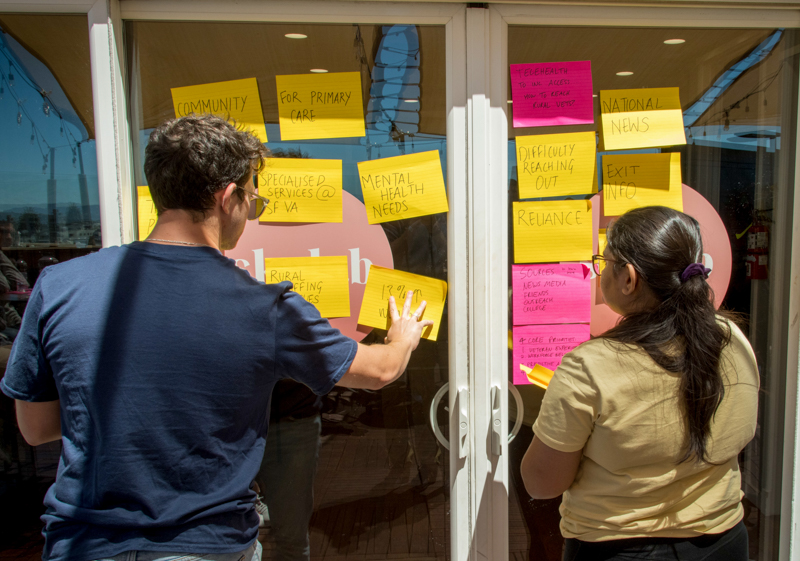 Two students creating a posit note wall with ideas.