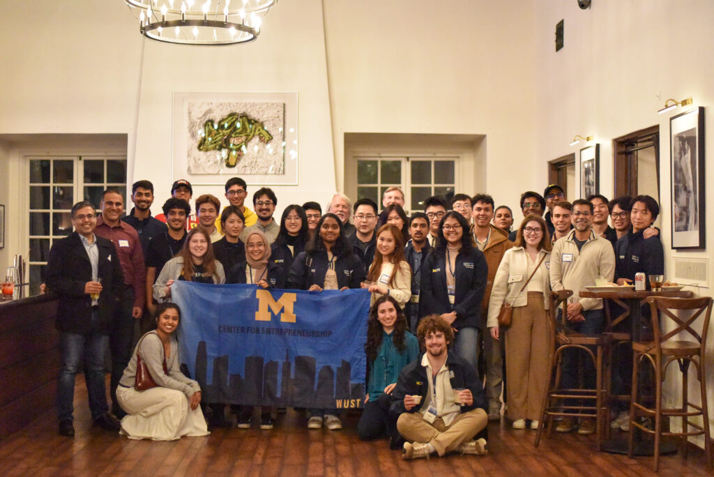 U-M students and alumni pose with a blue flag that reads 