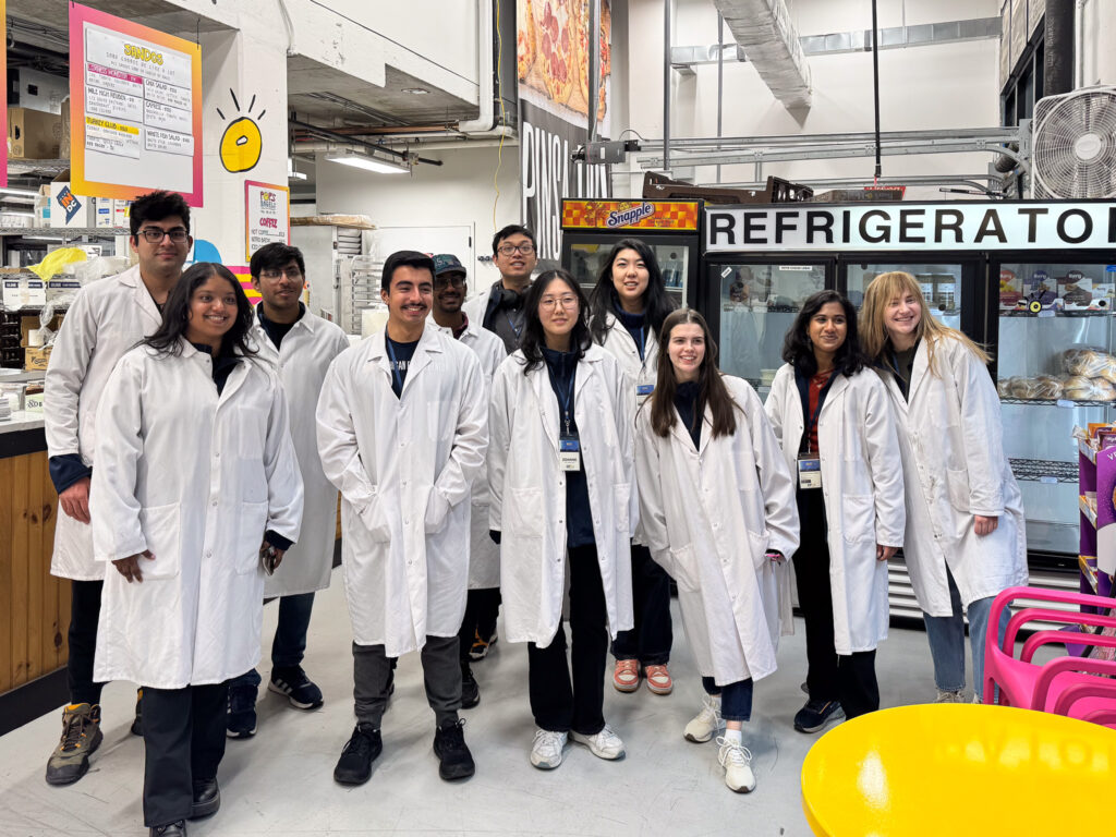 Students smile in white lab coats as they pose for a photo at Union Kitchen