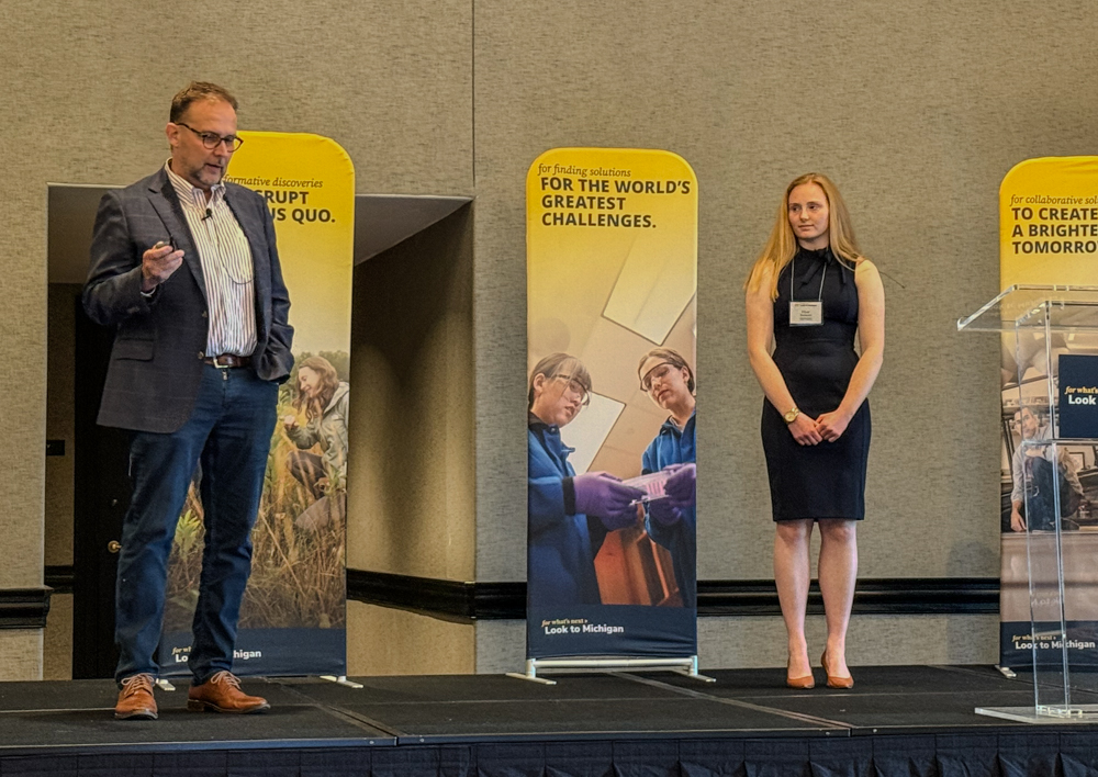 Cfe director kurt skifstad and alumni elyse sorraco on stage in Austin texas. Backdrop has yellow banners with funding images.
