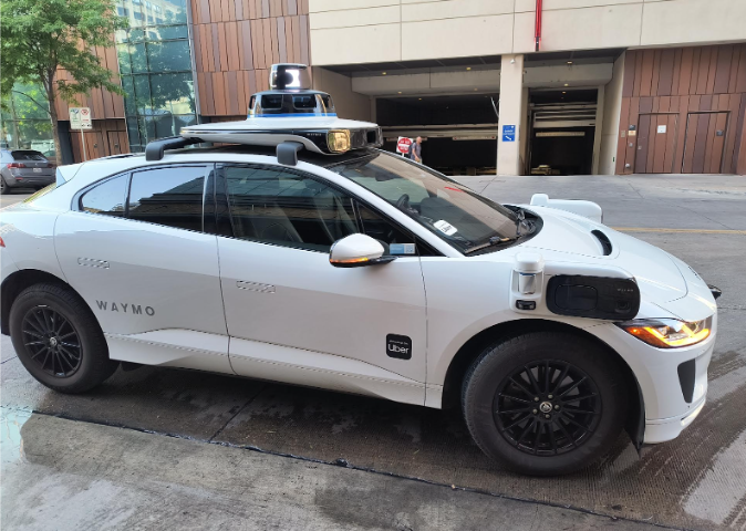 waymo self-driving vehicle in white, cameras are on the slides and the top