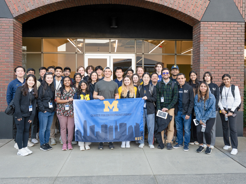 a large group of Students on a trek to San Francisco holding a center for entrepreneurship flag outside in front of a building