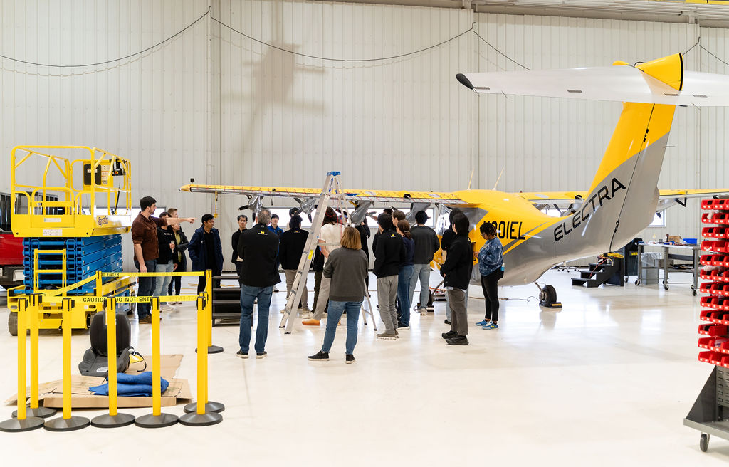 group of students in an airport hanger around an airplane