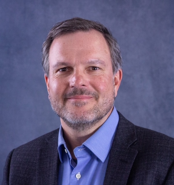 Jan Stegmann headshot with a slight beard & mustache wearing a bright blue shirt and a navy jacket
