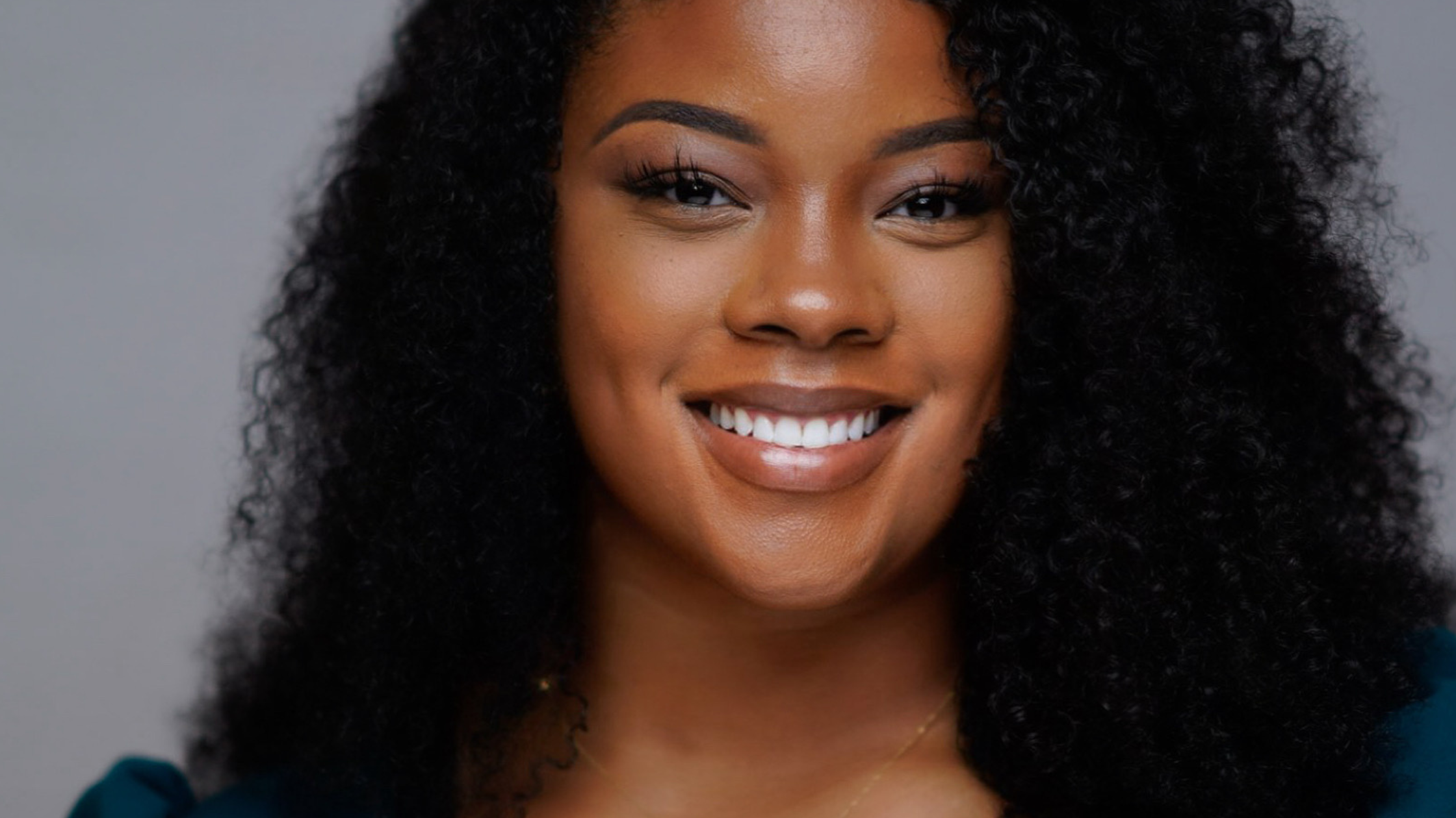 A close up of Tanisha as she smiles at the camera against a gray backdrop.