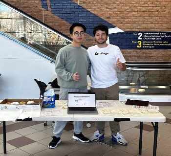 two students looking at the camera from behind a table at the duderstadt center