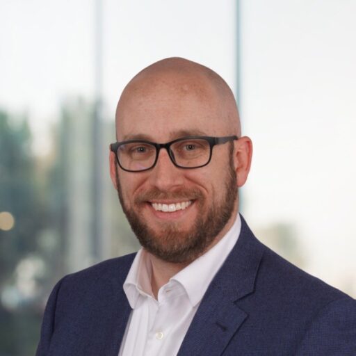 danny ellis headshot. A man wearing glasses a blue sport coat and white shirt. He has no hair on his head and a beard & mustache