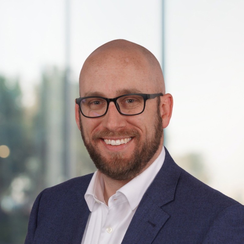 danny ellis headshot. A man wearing glasses a blue sport coat and white shirt. He has no hair on his head and a beard & mustache