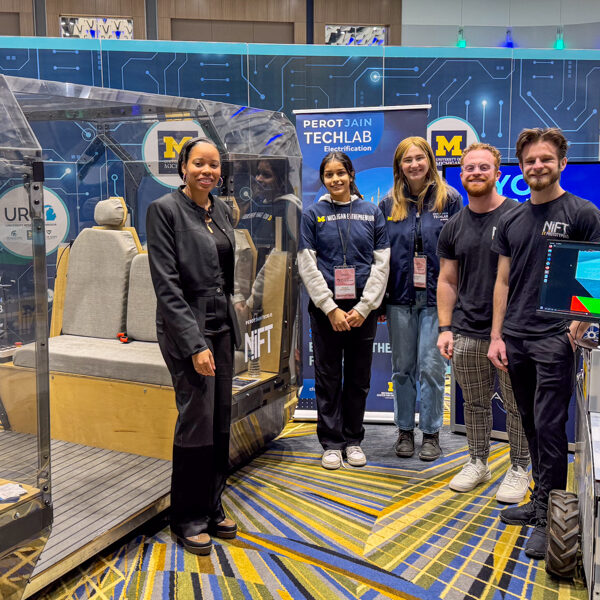 a team of students with Justine Johnson, Michigan’s Chief Mobility Officer. The students an justine are gathered in the U-M CFE student display at the detroit auto show around a NIft autonomous vehcile
