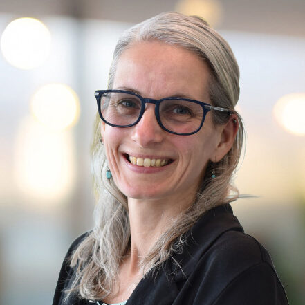 Dani Koniczek is a woman with light hair wearing glasses and a black jacket
