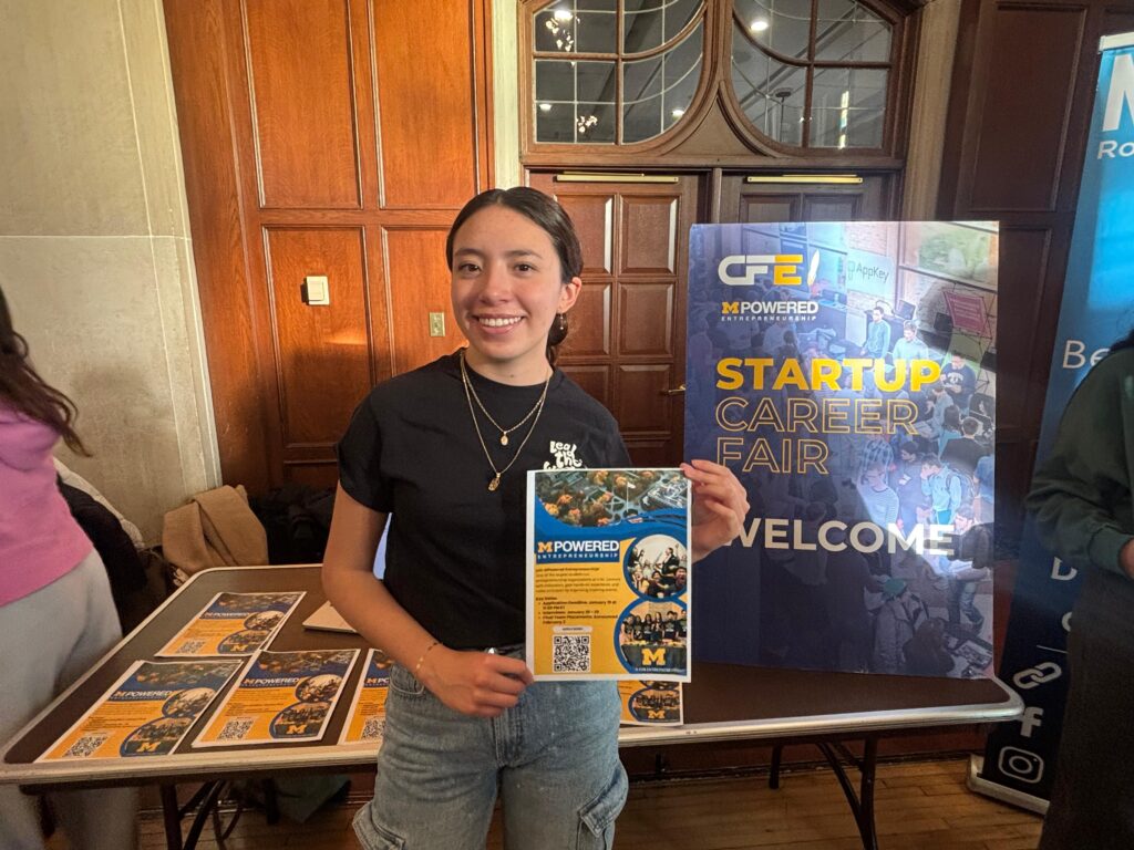 Ivana poses for a photo at a tabling event, where she is advertising CFE & MPowered's Startup Career Fair.