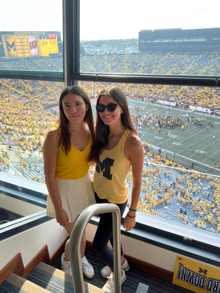 Ivana poses with a friend in the stands at a Michigan football game. She is dressed in maize for the game.