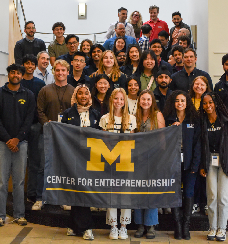 a large group of students, of all genders standing on staircase for a picture holding a Center For Entrepreneurship Flag