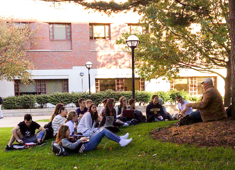 a group of students in the grove under a tree listening to their instructor