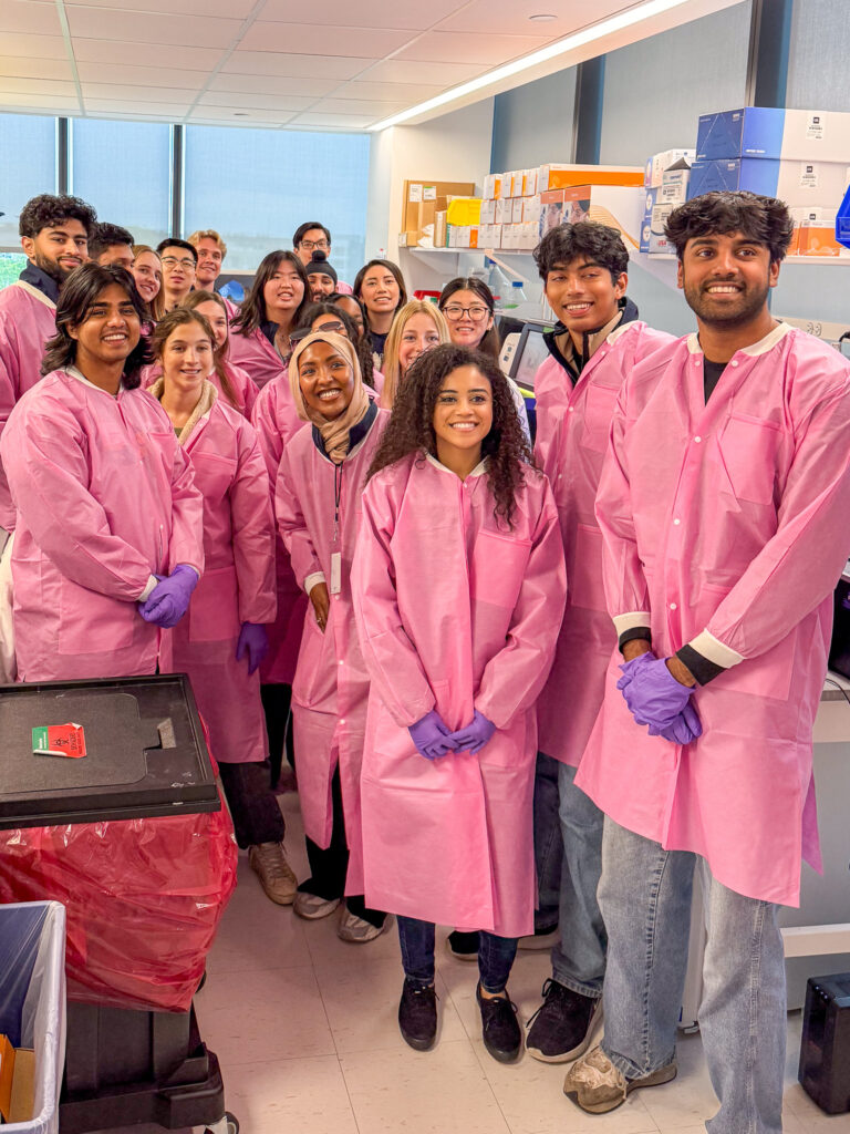 A group of students in pink lab coats in a laboratory