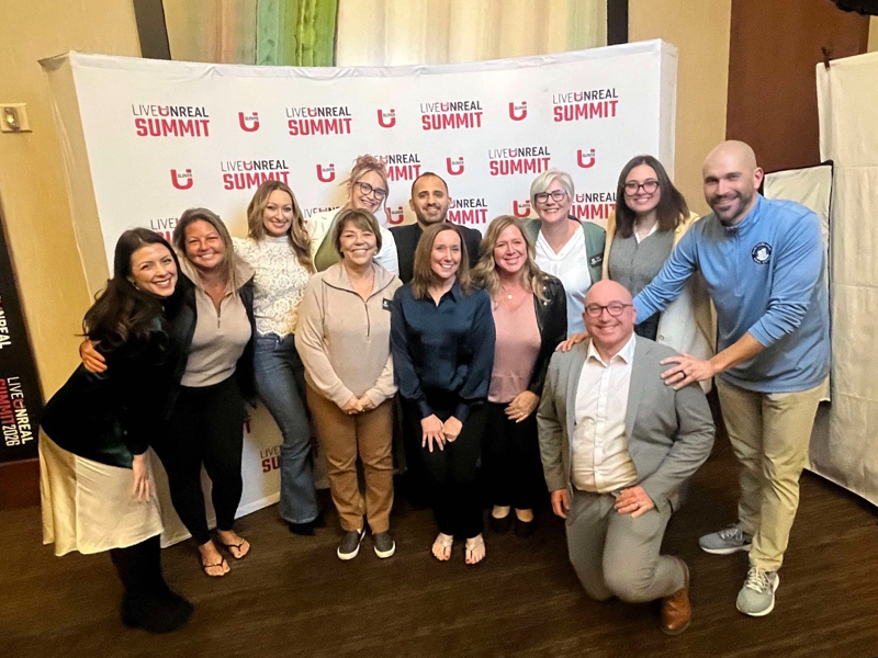 a group of men and women in front of the Live unreal summit backdrop