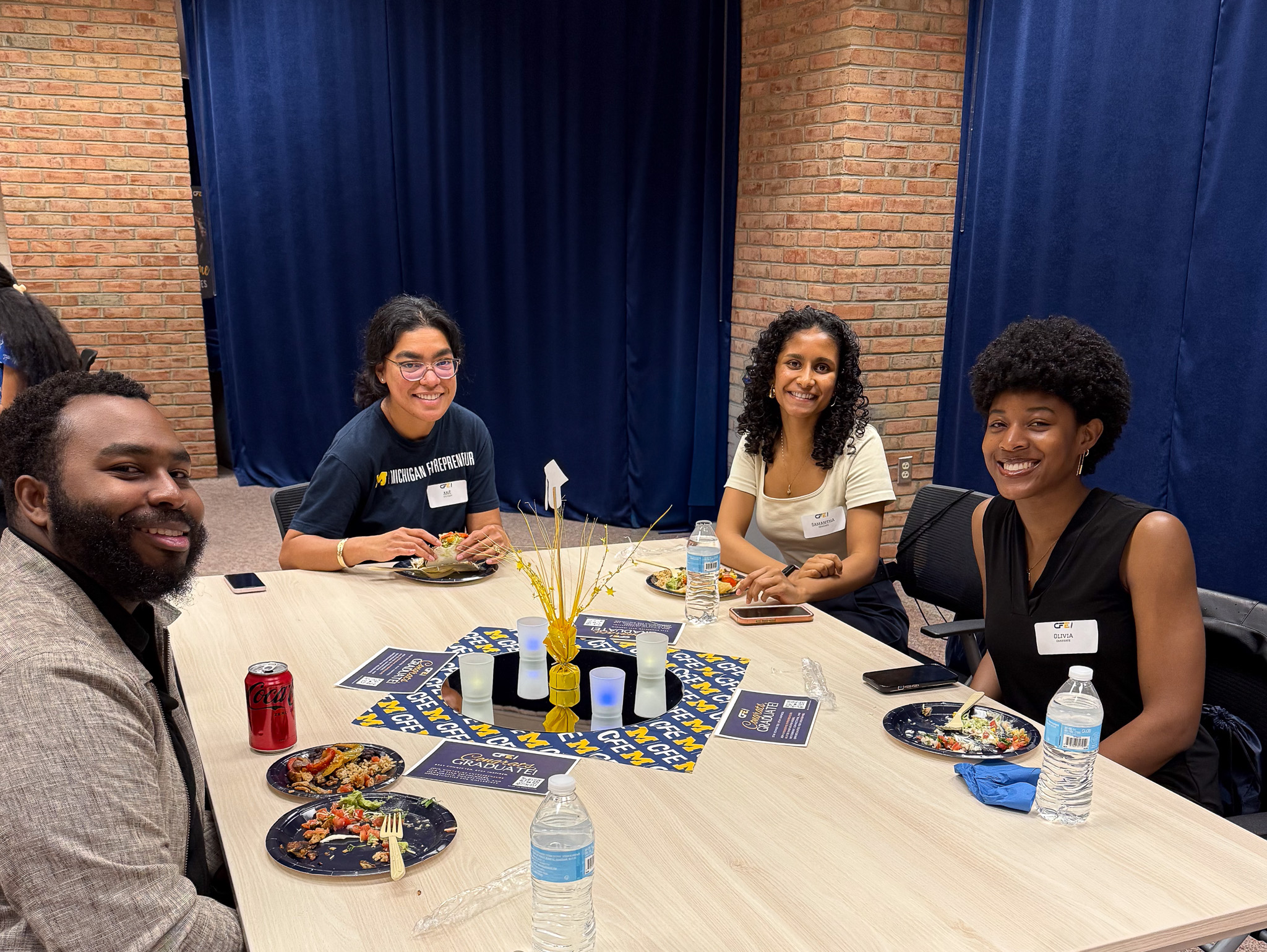 a group of students and staff sitting at a table at a grad party