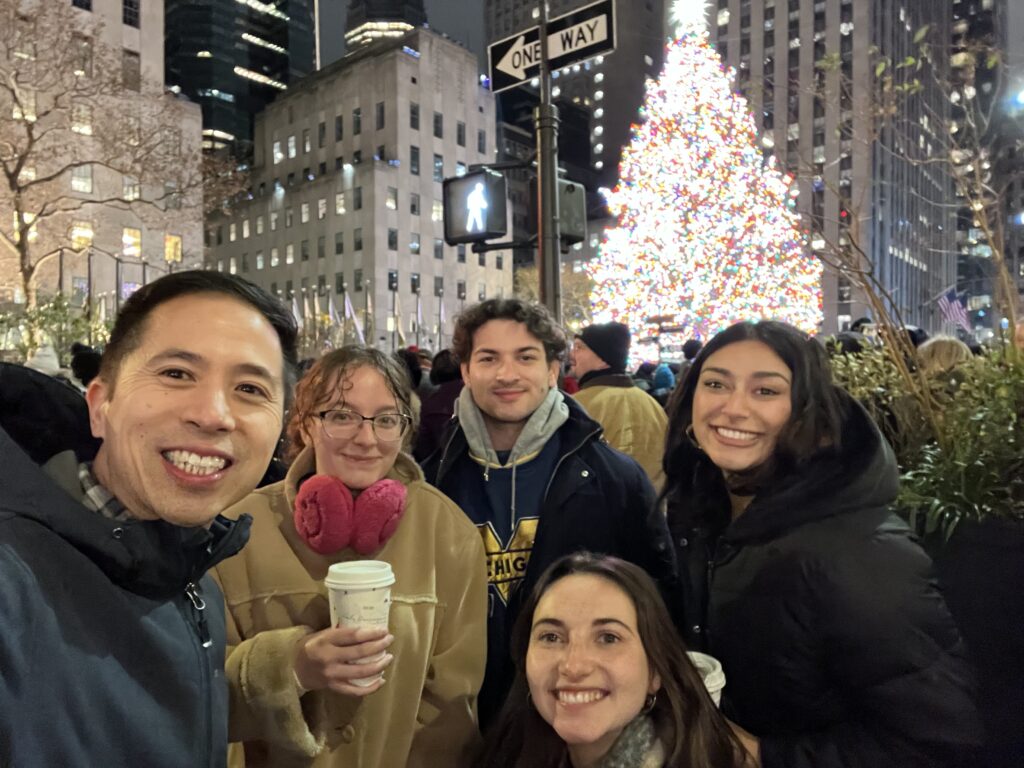 Michael poses with fellow students and instructor Moses Lee in front of a lit Christmas tree in what appears to be Downtown Detroit.