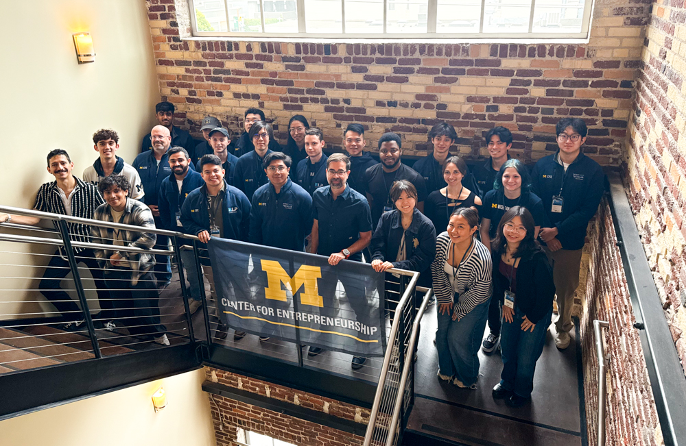 a group of students on a staircase smiling for the camera and holding a Center for Entrepreneurship flag