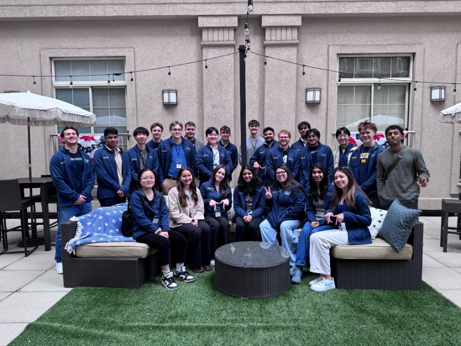a group of students standing and sitting around a table with twinkle lights in the background