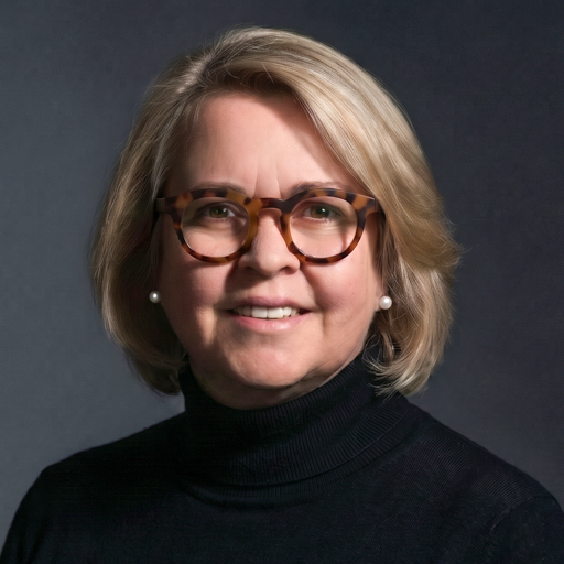 MariAnn Apley is a woman with short blond hair and glasses wearing a black turtleneck