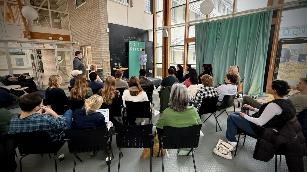 Students stand in front of signage reading "1, 2, 3 pitch!" while pitching their venture.