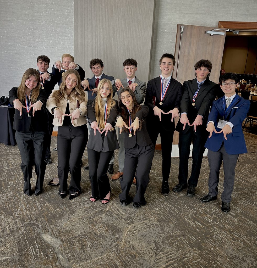 Julia poses with her DECA team. They are wearing medals and making an "M" with their hands, celebrating a win.