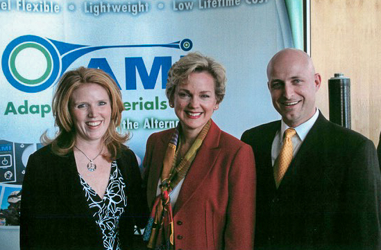 Aaron Crumm wearing a dark suit with a yellow tie, in a picture with ex-governor Jennifer Granholm 
