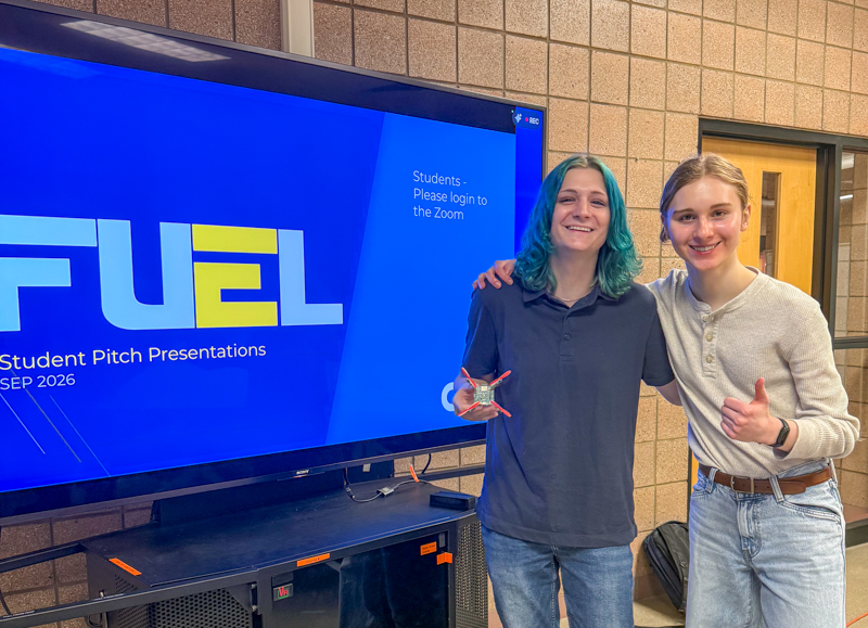 two women in front of a fuel sign showing off their prototype