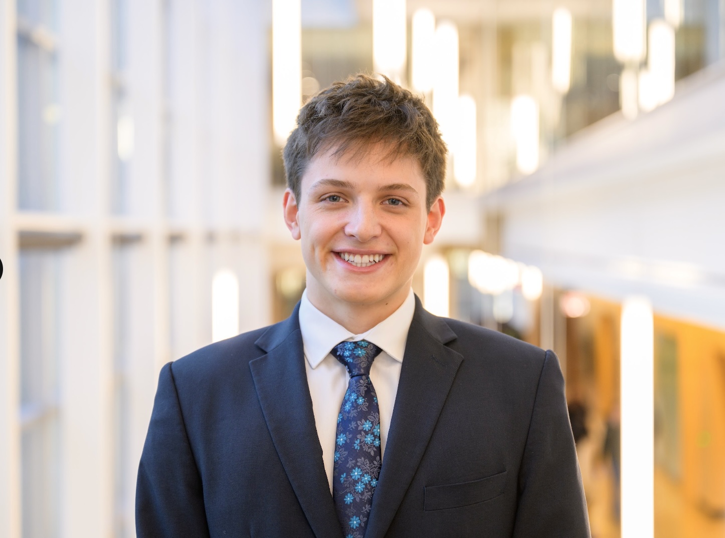 Isaac Gardner poses for a headshot. He wears a black suit and a blue tie.
