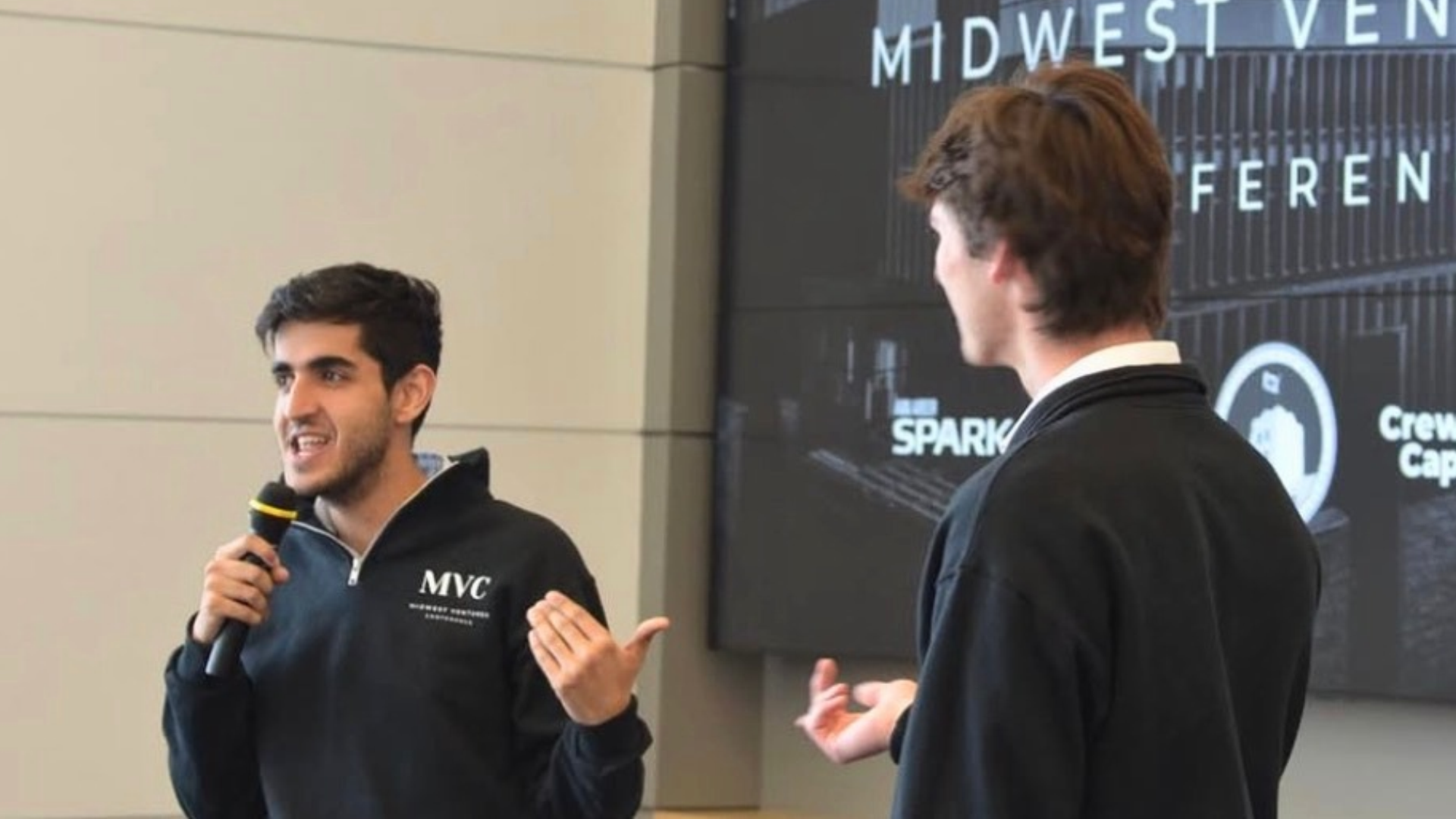Arjan holds a microphone and speaks in front of a slideshow.