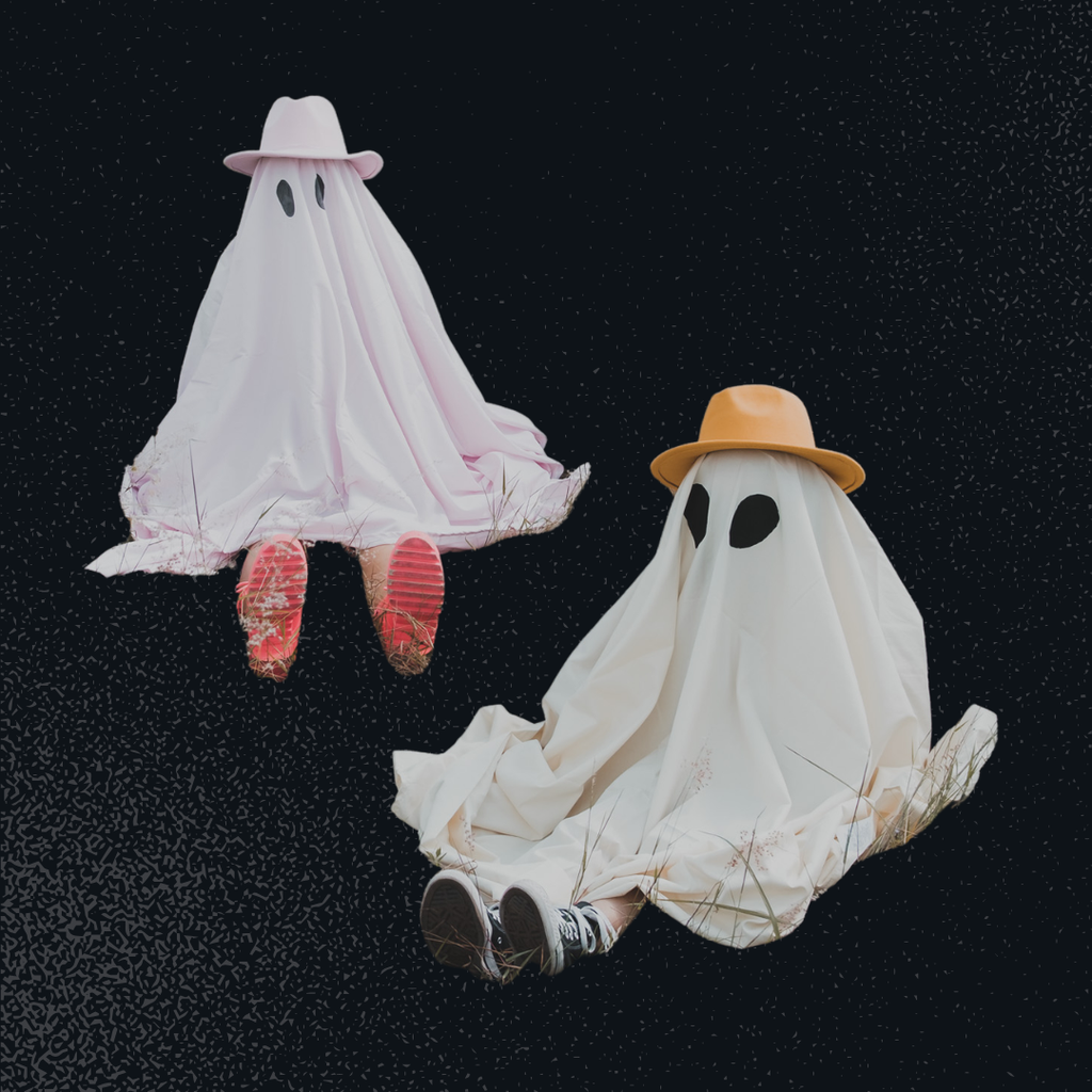 Two classic bedsheet ghosts are shown sitting on the ground wearing hats.